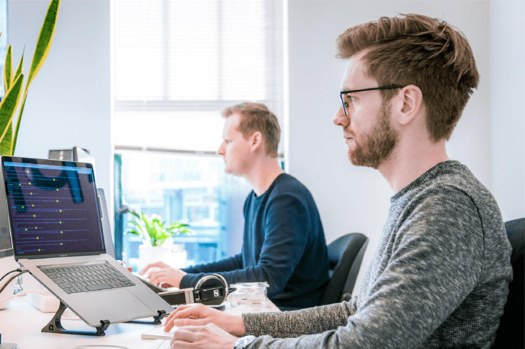 Two men collaborating on cloud security solutions while working on their laptops